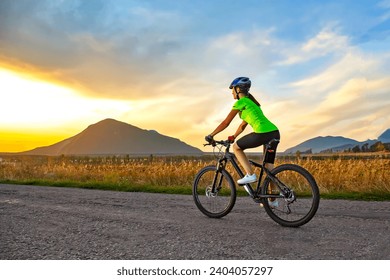 Beautiful girl cyclist riding a bike on the road towards the sunset. Nature and recreation. Hobbies and sports
