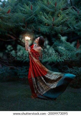 Beautiful girl dances. red national vintage dress flutter fly in wind. Indian woman holding in hands bright light fantastic beauty magical lotus flower. Backdrop nature summer green trees forest park.