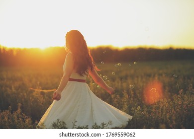 Beautiful girl dancing in a park in the sunset light. Soap bubbles. Happiness concept.