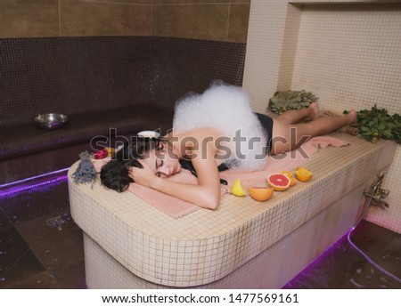 A beautiful girl with dark hair and a slender figure takes bath procedures in a Hammam, a bath attendant does massage, applies cosmetic oils and means to the skin of a slender young girl