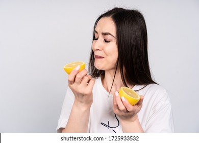 Beautiful girl with dark hair in white t-shirt eating fresh sour lemon.