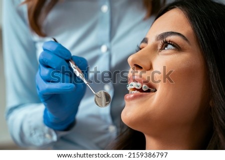 Beautiful girl with dental braces at dental checkup, smiling while dentist holding dental mirror ストックフォト © 