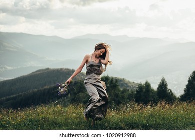 A beautiful girl in a developing dress, dances among the tops of mountains with a bouquet of flowers in her hands and a wreath on her head. Mountains on the horizon