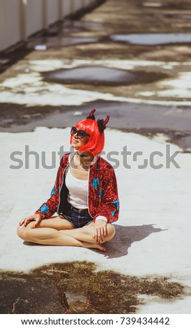 Beautiful girl devil sitting on city background near the puddle with his reflection. In anticipation of Halloween. Portrait. Wears black sunglasses