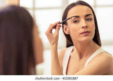 Beautiful Girl Is Doing A Makeup, Retouching Eyebrows While Looking At The Mirror