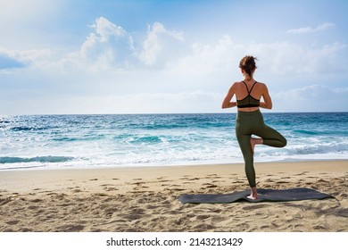 A beautiful girl is doing yoga on the beach near the sea. A girl in a green tracksuit does yoga exercises on the sand, and against the backdrop of the sea surf and a beautiful sky. - Powered by Shutterstock