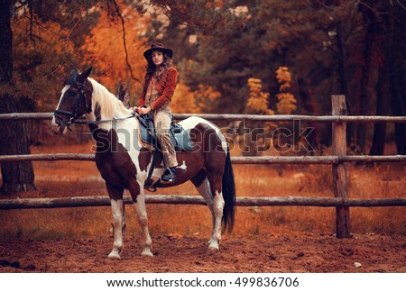 Beautiful girl dressed as an American cowboy on a horse in the paddock, golden autumn