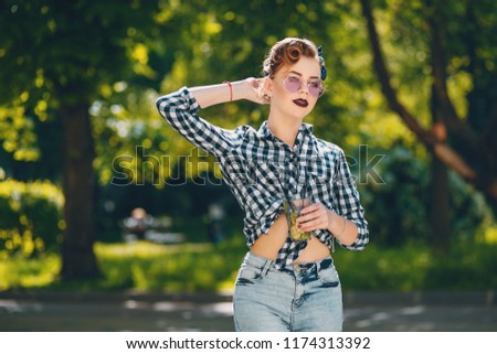 beautiful girl dressed in a pin up style in park with cocktail