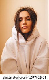 Beautiful girl dressed in sports clothes sitting and relaxing. Brunette with long hair posing. She is dressed in white hoodie. Sexy woman look at camera. Brunette woman looks proud and arrogant. 
