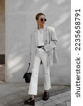 beautiful girl dressed in white flared jeans, gray jacket, t-shirt, black patent leather loafers, bag, sunglasses, belt, hair gathered in tail, accessories, stylish fashion outfit, lifestyle model