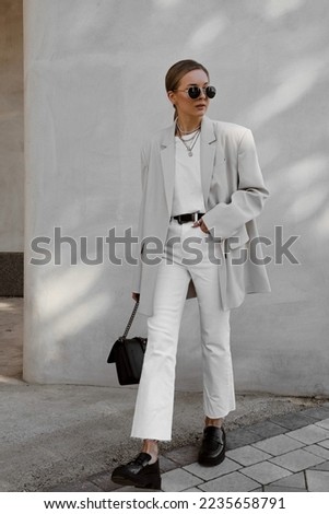 beautiful girl dressed in white flared jeans, gray jacket, t-shirt, black patent leather loafers, bag, sunglasses, belt, hair gathered in tail, accessories, stylish fashion outfit, lifestyle model