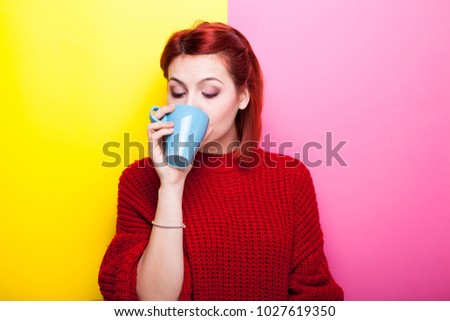 Beautiful girl drinking coffee from a blue mug on two colored background in yellow and pink