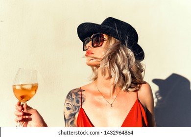 Beautiful girl in drinks Aperol Spritz wine from a glass in a restaurant, a cafe, has a good weekend, a stylish fashionable woman, a brunette young, emotional, outdoor close up hipster portrait