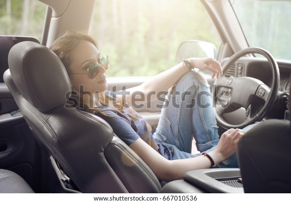 Beautiful girl, the\
driver, sits behind the wheel of a car with sunglasses on and\
resting in the Parking\
lot