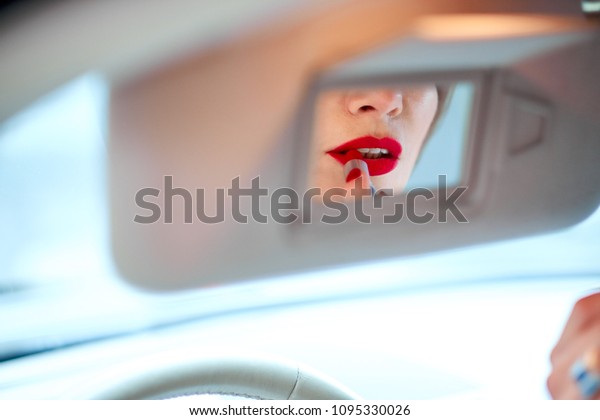 Beautiful girl driving a car paints lips with\
red lipstick.