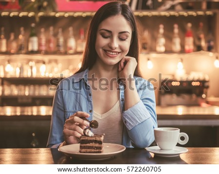 Beautiful girl is eating cake and smiling while sitting at the cafe