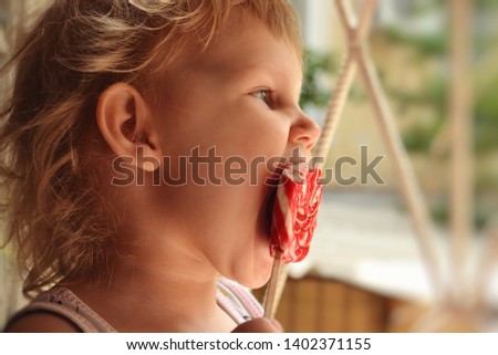 Beautiful girl eating candy. A child with blond curly hair. Candy on a stick. 