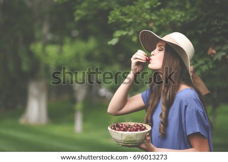 Beautiful girl eating fresh cherries outside in the garden