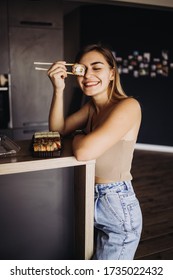Beautiful girl eats sushi with red fish, keeps sushi sticks, large rolls lie on a plate