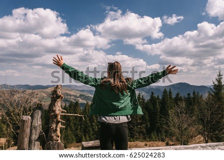 Beautiful girl enjoys the view in beautiful mountains. Snow on tops of mountains, spring grass, air, clouds, sky. Concept photo travel and tourism. Back view