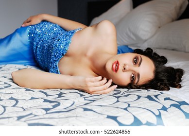 beautiful girl in evening blue dress lies on a bed and looking at the camera
