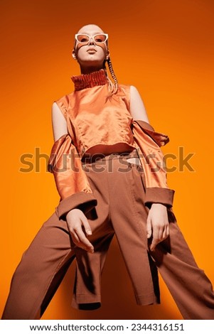 Beautiful girl fashion model posing in designer clothes from the summer collection on an orange studio background. Fashion photo.
