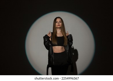 Beautiful girl in fashionable casual rock clothes with a top and a leather jacket on a dark background in a light circle - Shutterstock ID 2254996367