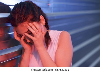 Beautiful girl feeling head pain, stress and disorientation. Holding her hands near her face. Outdoors, leaning on a steel wall. Taken using blue and red flashes. - Shutterstock ID 667630531