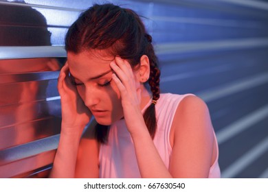 Beautiful girl feeling head pain, stress and disorientation. Holding her hands near her face. Outdoors, leaning on a steel wall. Taken using blue and red flashes. - Shutterstock ID 667630540