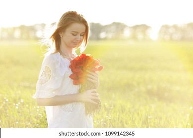 beautiful girl in a field with a bouquet of red poppies at sunset