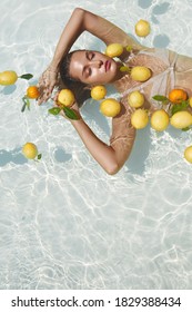 Beautiful Girl Floating On Water With Fresh Tropical Fruits At SPA. Young Woman's With Sexy Slim Body Portrait In Pool With Citrus. 