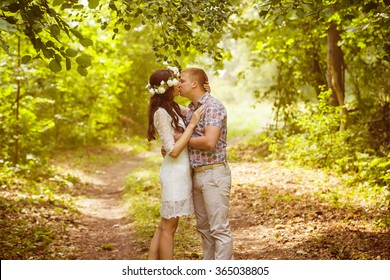 Beautiful girl with flowers circlet is kissing young boyfriend at green outdoors spring background.