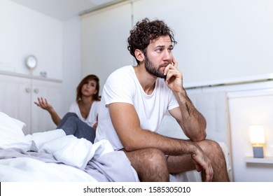 Beautiful girl and a frustrated man sitting in bed and not looking at each other. Upset couple ignoring each other. Worried man in tension at bed. Young couple angry with each other after a fight.
