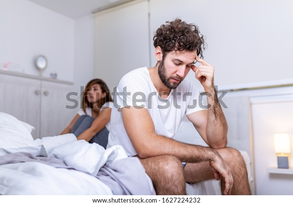 Beautiful girl and a frustrated man sitting in bed
and not looking at each other. Upset couple ignoring each other.
Worried man in tension at bed. Young couple angry with each other
after a fight.