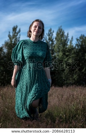 a beautiful girl in a gorgeous green dress is dancing on a warm summer day in an unmown meadow and enjoying the beautiful weather