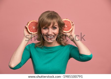 A beautiful girl with grapefruits in her hands, a blonde in a green dress holds halves of a grapefruit in her hands, beauty, vitamins, healthy skin.