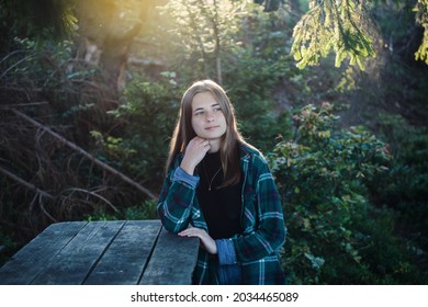Beautiful Girl with Green Plaid Shirt sitting in the Woods at a Wooden Table