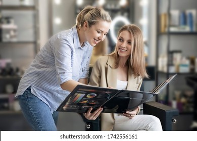 A beautiful girl hairdresser shows the client a color palette and helps to choose the color that suits her hair. A young girl in a beauty salon chooses a hair color. Concept of a beauty salon.