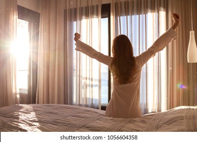 The beautiful girl has woken up in the morning at sunrise, reaching up your hands, sitting on the bed in the bedroom.