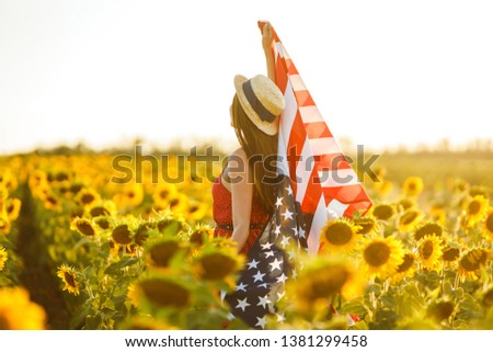 Beautiful girl in hat with the American flag in a sunflower field. 4th of July. Fourth of July. Freedom. Sunset light The girl smiles. Beautiful sunset. Independence Day. Patriotic holiday. 
