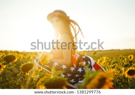 Beautiful girl in hat with the American flag in a sunflower field. 4th of July. Fourth of July. Freedom. Sunset light The girl smiles. Beautiful sunset. Independence Day. Patriotic holiday. 