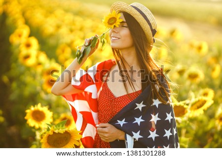 Beautiful girl in hat with the American flag in a sunflower field. 4th of July. Fourth of July. Freedom. Sunset light The girl smiles. Beautiful sunset. Independence Day. Patriotic holiday.