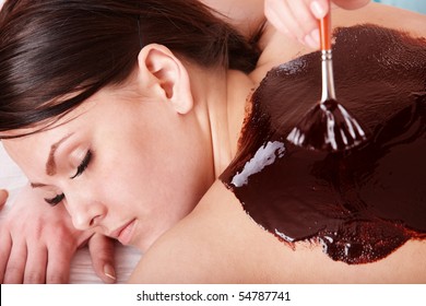 Beautiful girl having chocolate facial mask apply by beautician.