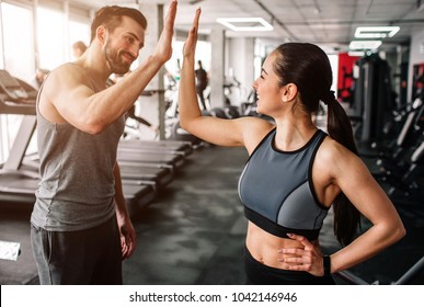A beautiful girl and her well-built boyfriend are greeting each other with a high-five. They are happy to see each othr in the gym. Young people are ready to start their workout. - Powered by Shutterstock