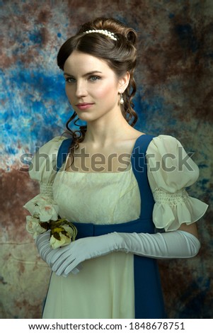 Beautiful girl in a historical dress in the Empire style of the early 19th century on an unusual blue background with streaks and flowers