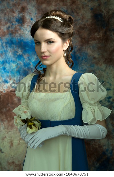 Beautiful girl in a historical dress in the
Empire style of the early 19th century on an unusual blue
background with streaks and
flowers