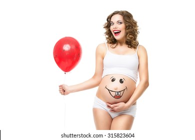 Beautiful Girl Holding Air Balloon And Holding Her Pregnant Belly With Smily Funny Face Drawn On It. Isolated Over White Background.