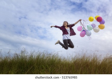 Beautiful girl holding balloons Jumping in prairie grass. On a clear day