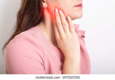 Beautiful girl holding her hand on the lower jaw of the tooth, which has an inflamed tooth nerve, dental abscess. Close-up