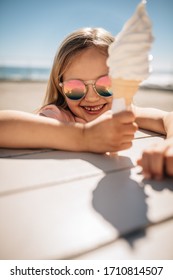 Beautiful girl holding a ice cream over a beach boardwalk. Young girl wearing sunglasses at the beach eating icecream on a summer day.